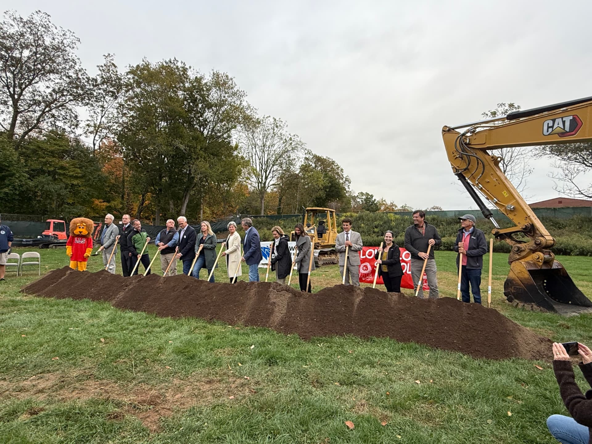 October 2025 — Town officials and board members line up with ceremonial shovels and Leo the Lion