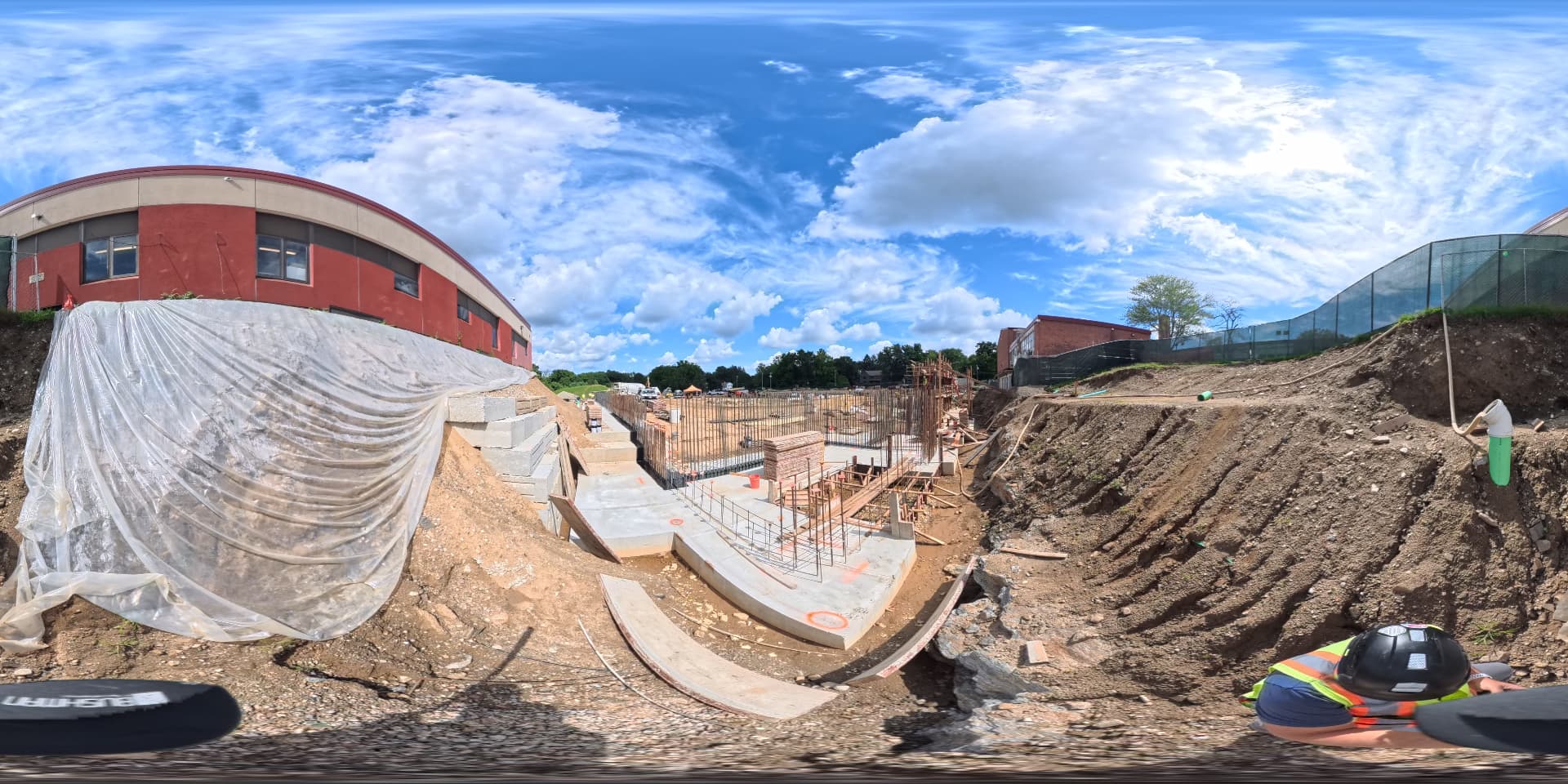 September 2026 — Foundation footings and rebar installation alongside the existing school, with the terraced slope covered for erosion protection