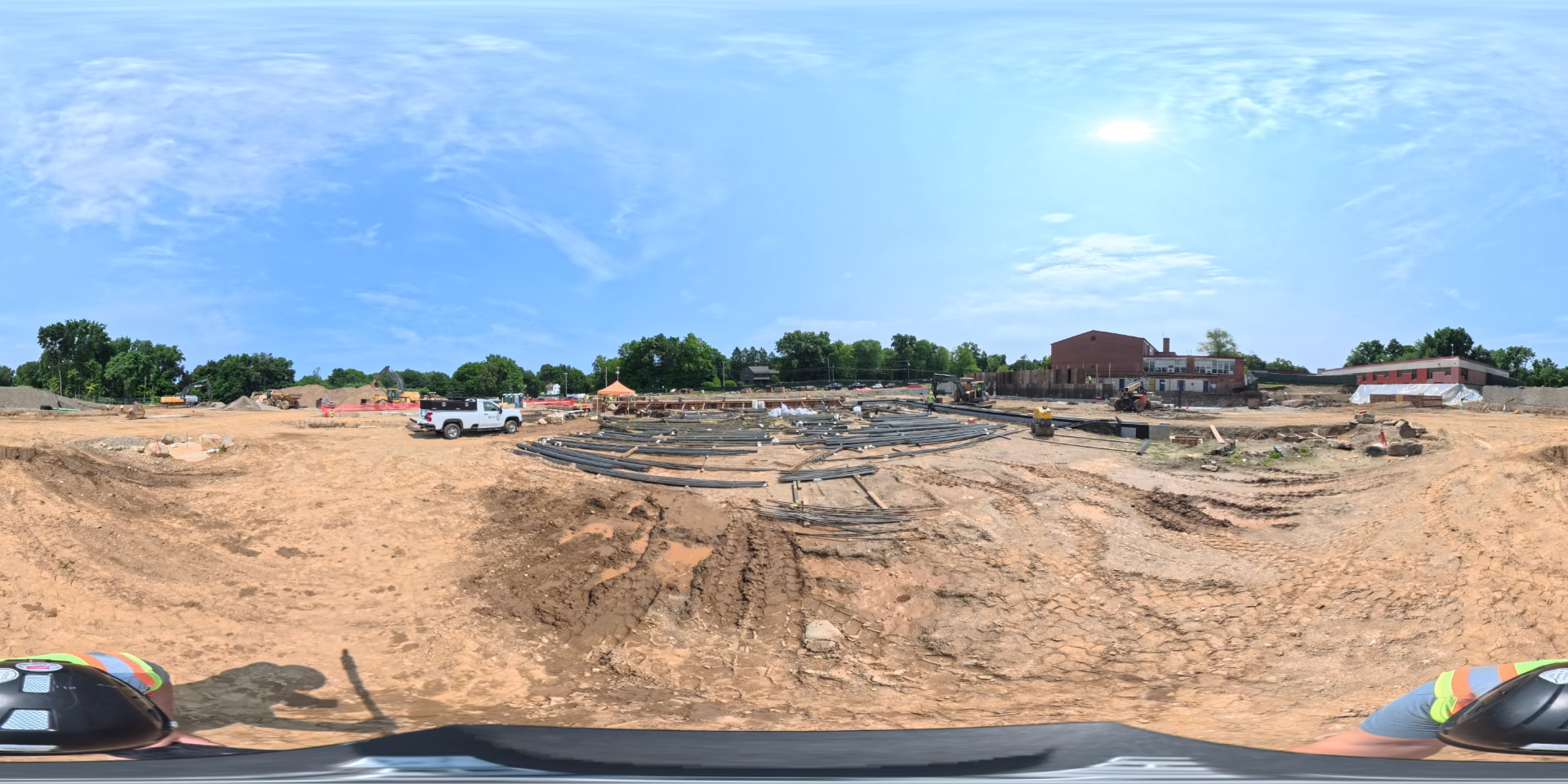 August 2026 — Bundled conduit and utility piping staged across the graded pad ahead of underground installation